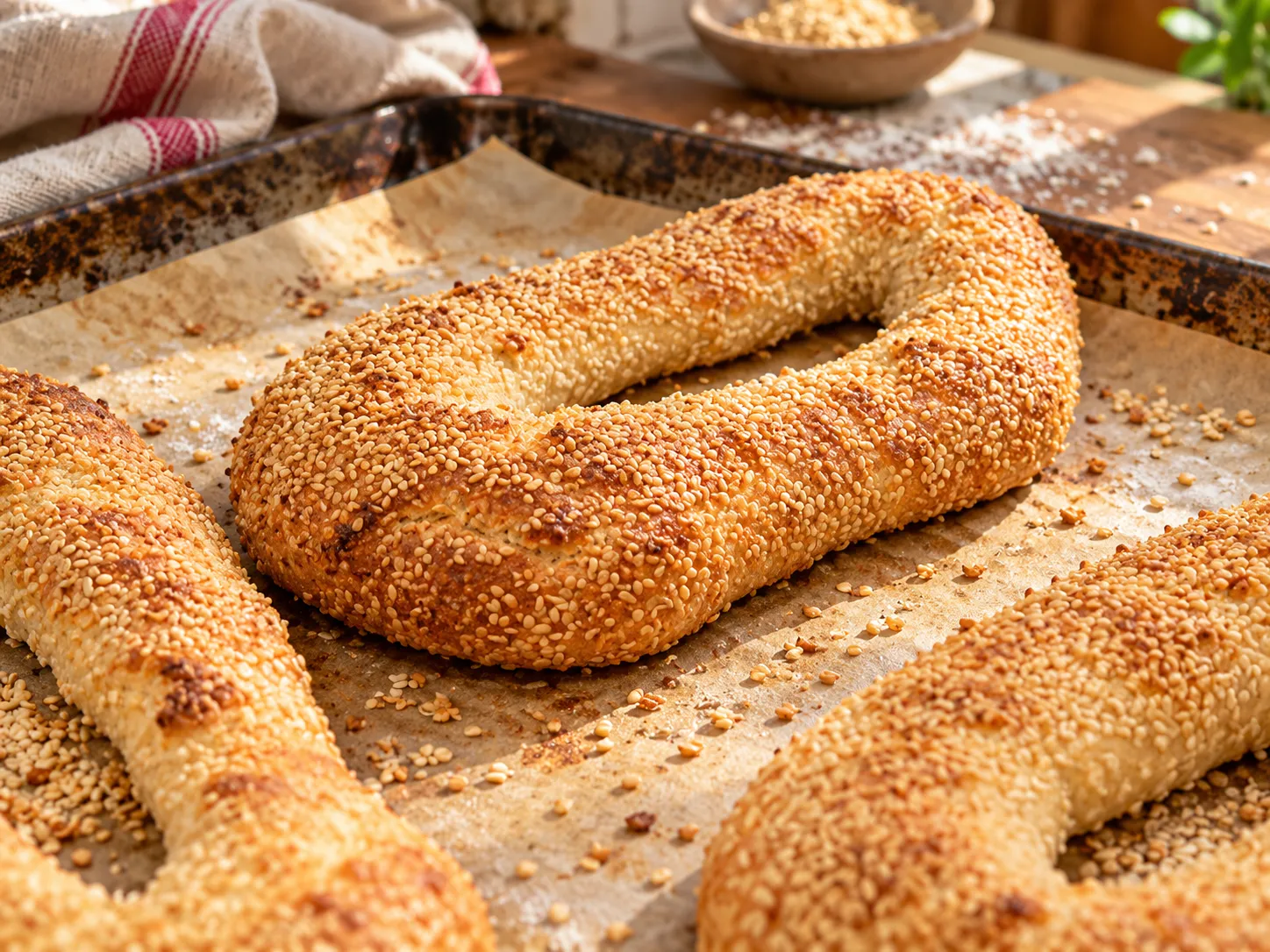 Long Jerusalem bagels covered in sesame seeds on a baking sheet